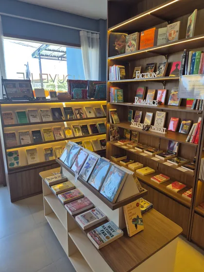 Inside Nouvelle: lit timber shelves labelled Fiction, Romance and Self-Development, a front table of face-out books, and the window with the Nouvelle lettering