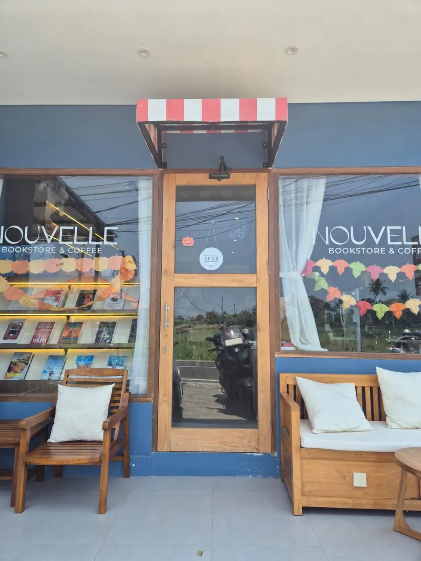 Nouvelle's entrance on Jalan Pantai Seseh: the striped awning over the timber door, Nouvelle Bookstore & Coffee lettering on both windows, books lit in the window display and a bench with cream cushions on the porch