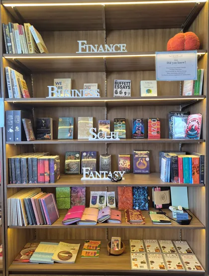 A lit timber bookcase at Nouvelle labelled Finance, Business, Sci-Fi and Fantasy, above shelves of notebooks, batik pouches, bookmarks and cookbooks